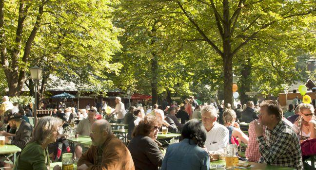 People relax outdoor on a beautiful October day, sitting in the sun, drinking beer and eating Bavarian traditional food in one of the many open air seasonal restaurant (Biergarten) of the Englischer Garten in Munich.