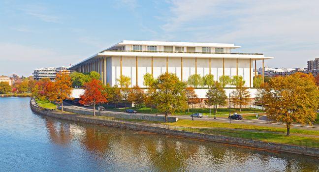 Modern building of Kennedy Center and colorful trees are reflected in Potomac River.