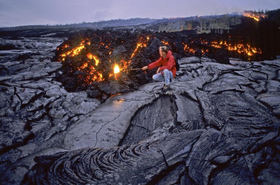 A volcanologist enters a glowing methane gas death zone where slow moving pahoehoe lava speads across the landscape and heads to the Pacific, exploding trees in its path. Hawaii Volcanos National Park