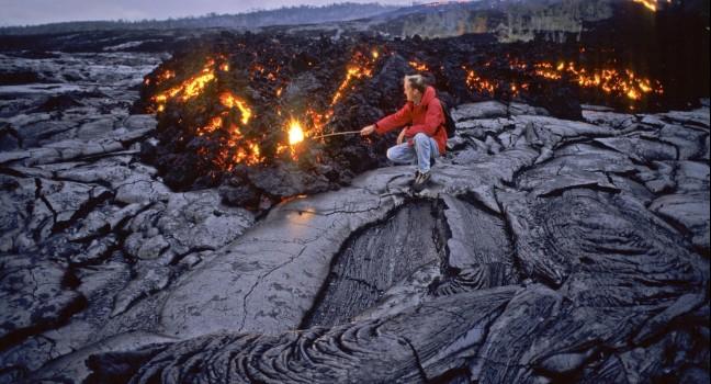 A volcanologist enters a glowing methane gas death zone where slow moving pahoehoe lava speads across the landscape and heads to the Pacific, exploding trees in its path. Hawaii Volcanos National Park