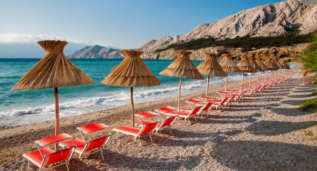 Sunshades and orange deck chairs on beach at Baska - Krk - Croatia