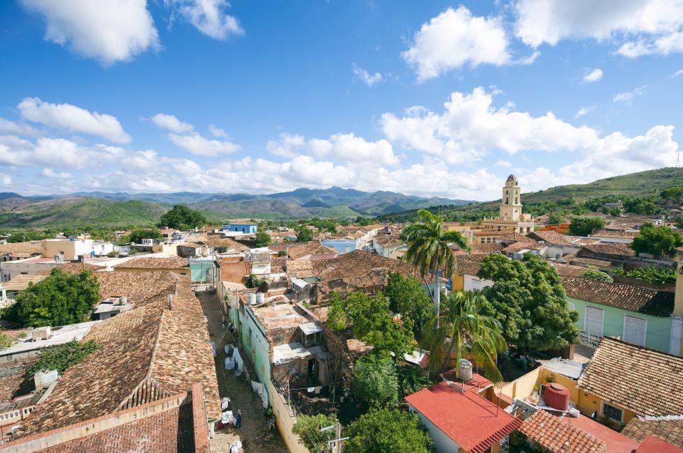 White clouds float in blue sky above the terra cotta rooftops of the historic colonial architecture in the UNESCO heritage center of Trinidad, Cuba. 