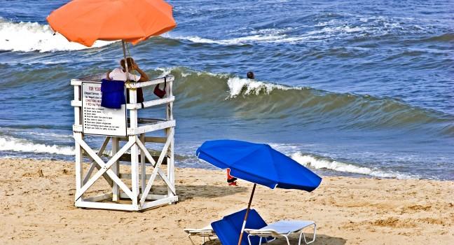 Female lifeguard at her post on Virginia Beach watching a lone swimmer in the ocean surf.