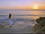 lovely hispanic lady in white dress watches sunrise at the beach;