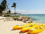 Three yellow kayaks and paddles sit on the tropical white sandy beach town of Riviera Maya, Mexico 