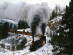 On a wintry curve of iron rails, coal-fired engines cough plumes of smoke and tug their locomotive burden across the Rocky Mountains