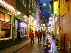 Bars and coffee shops on the street full of tourists at night in famous Red Light District in Amsterdam, Netherlan ds.