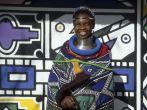 Neck-stretching brass coils announce marrigage as do a beaded jocolo wedding apron that mirrors the primary colors of the decorations hand painted by the mguni-speaking Ndebele.  Bronkhorstspruit, South Africa