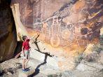 A boy shows his hand on the wall with petroglyphs. Dinosaur National Monument (USA. Utah)