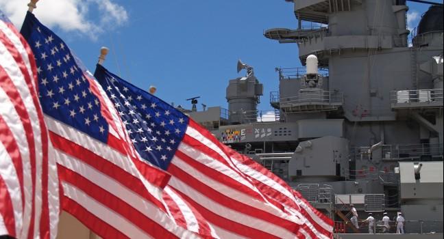 US flags flying beside the Battleship Missouri in Pearl Harbor, Honolulu, Oahu, Hawaii with 4 sailors walking on deck.