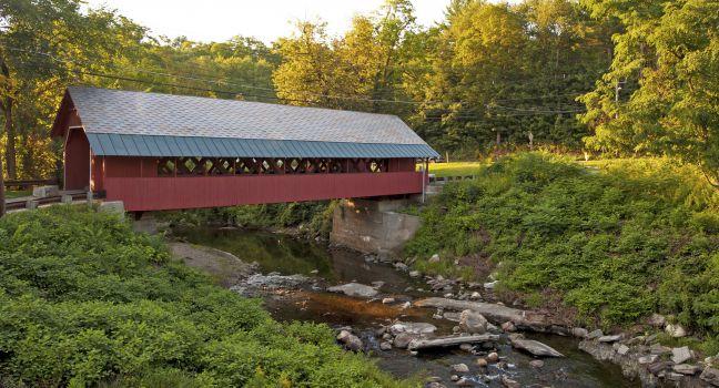 Creamery covered bridge built in 1879 in Brattleboro Vermont. Beautiful historic red covered bridge with a flowing stream of water below it.