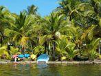 Tropical coast with coconut palm trees and colorful kayaks with a small boat awaiting tourists, Caribbean, Carenero island, Bocas del Toro, Panama.