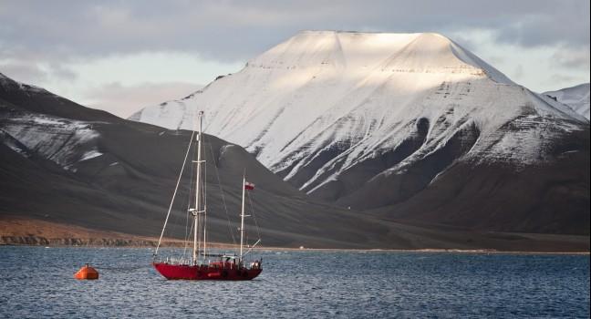 Polish red sailing boat to the buoy in Adventfjorden, in front of Longyearbyen port, snowy mountain background, horizontal