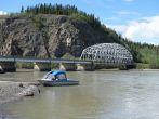 A scenic picture of a bridge in alaska with a small boat on a river.