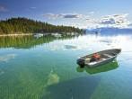 My lonely little fishing  boat setting on the Calm clear water in lake Tahoe, with Trees and Mountains in the background; 